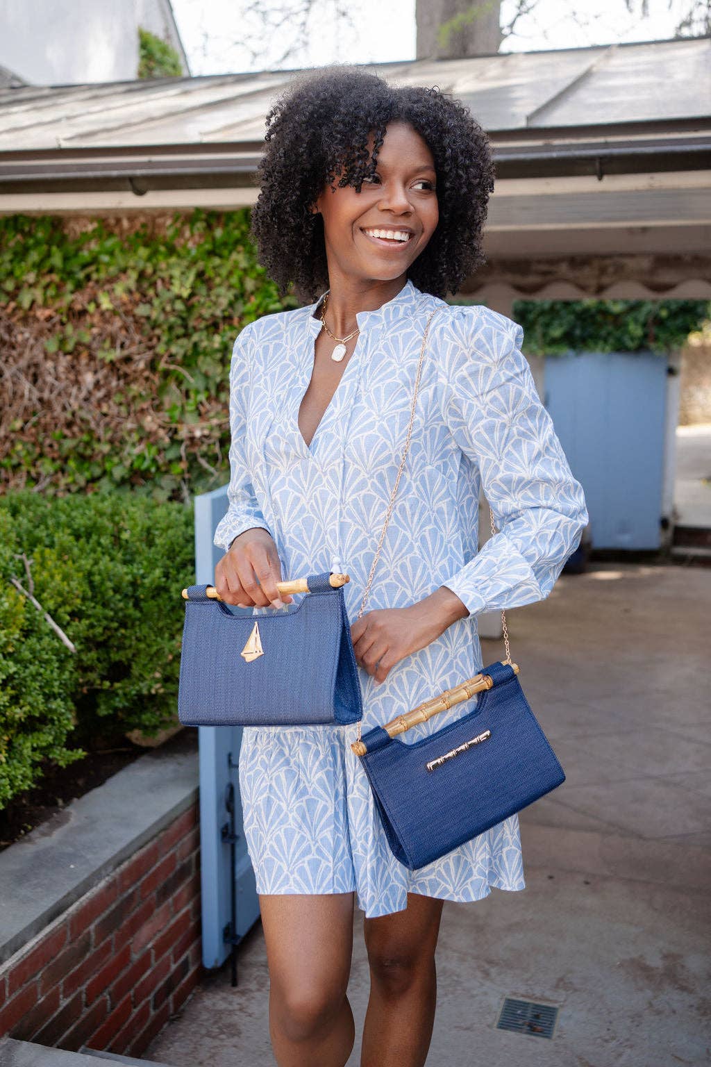 Woman in a light blue dress holding two blue handbags outdoors.
